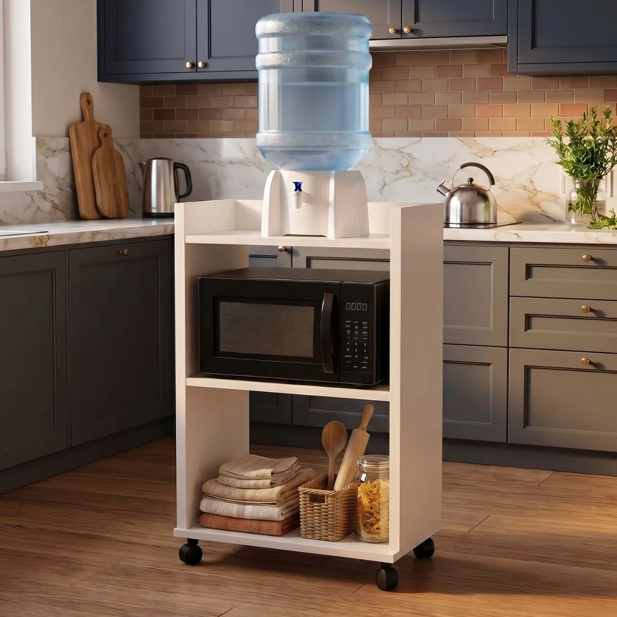 Mueble multiuso blanco con ruedas en una cocina, con un bidón de agua con dispenser arriba, un microondas en el estante del medio y repasadores abajo